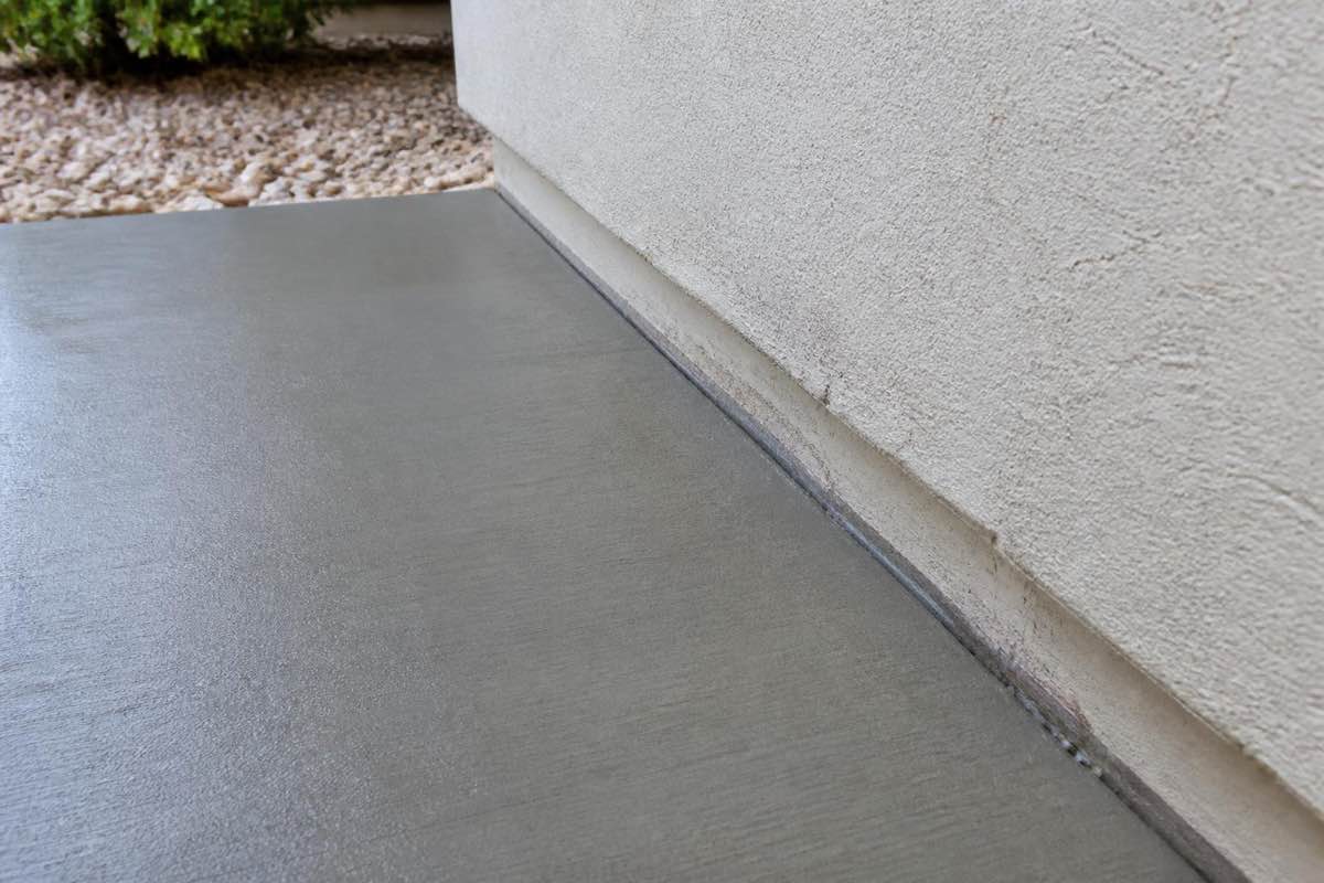 Newly poured concrete meeting the stucco wall of a house at the foundation
