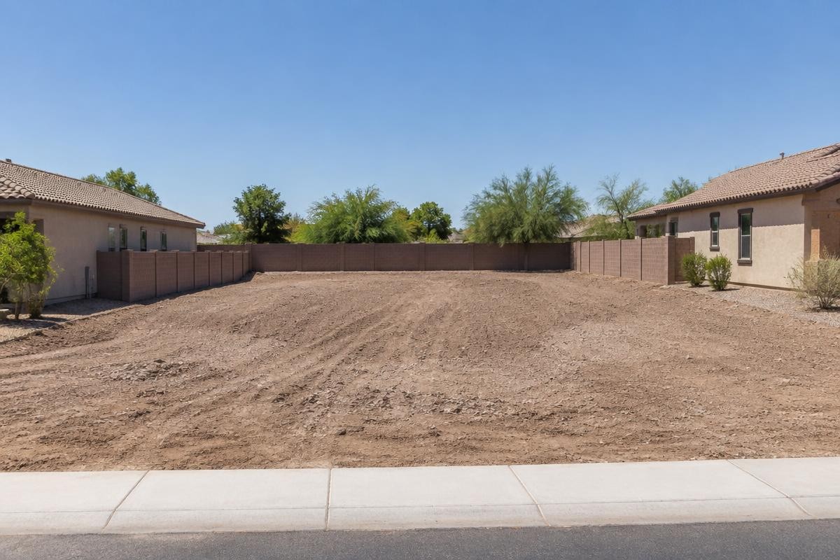 A graded, empty building plot sitting between two completed houses on a new street