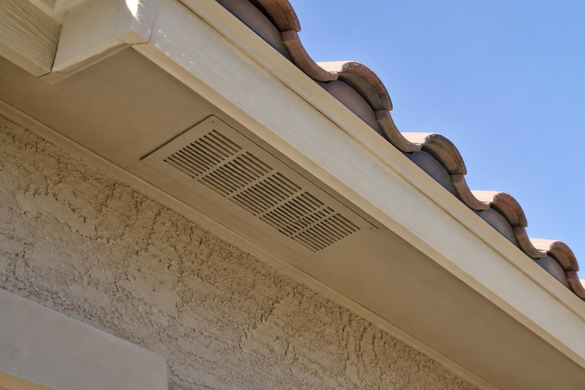 A close-up of a perforated soffit vent under the eaves of a concrete tile roof