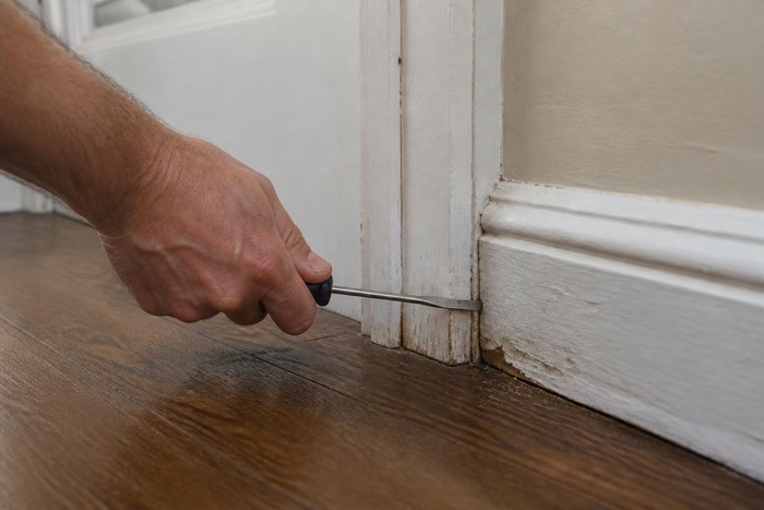 Inspector probing the base of a painted door frame with a screwdriver