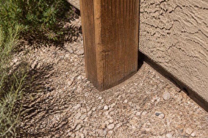 Timber fence post set directly into gravel against a stucco wall