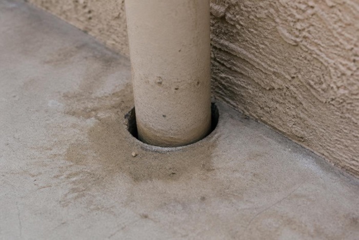 Gap around a pipe passing through a concrete slab at the base of a stucco wall